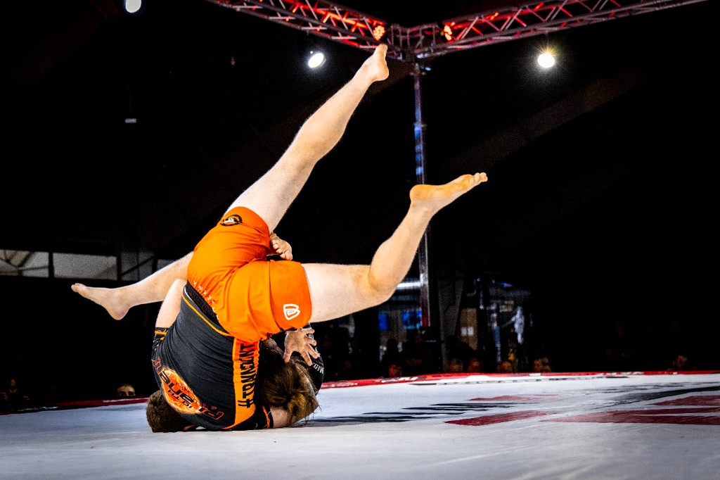 Dynamic judo-style throw during grappling competition with audience visible