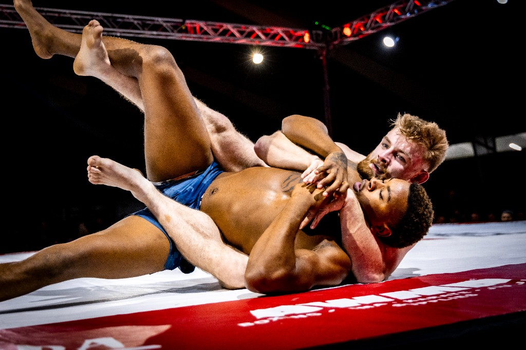 Rear naked choke scramble with two athletes on mat during grappling match