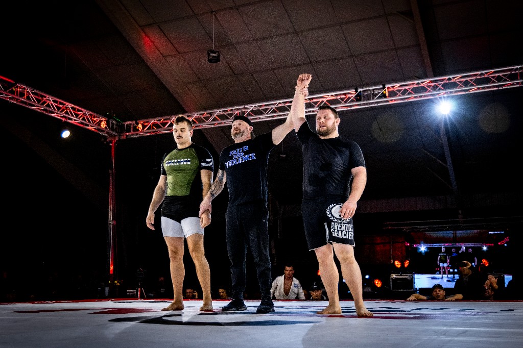 Referee raising winner's hand after combat sports bout with crowd in background