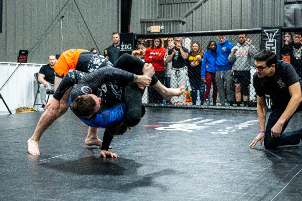 Wide shot of grappling takedown across mat with corner branding